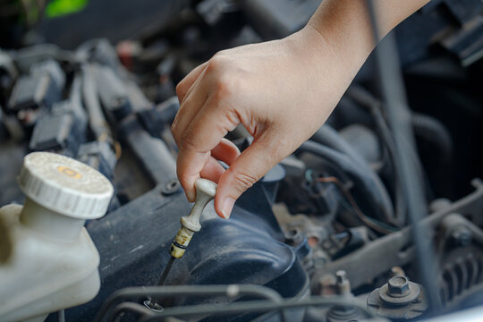 Close up of a  hand of woman pulling an engine oil dipstick to inspect oil level