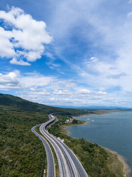 Drone aerial view of a highway running beside a reservoir with lush green mountains, Transportation infrastructure and renewable energy concept
