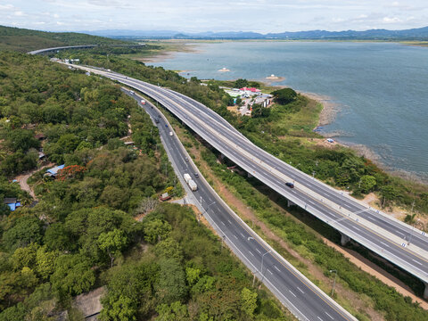 Drone aerial view of a highway running beside a reservoir with lush green mountains, Transportation infrastructure and renewable energy concept