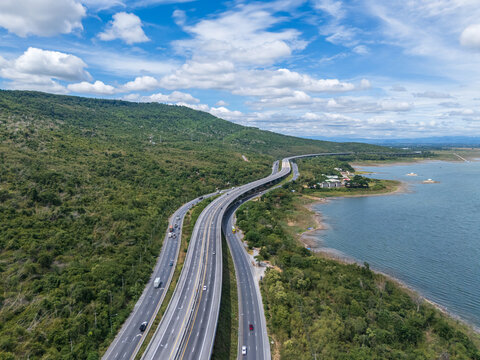 Drone aerial view of a highway running beside a reservoir with lush green mountains, Transportation infrastructure and renewable energy concept