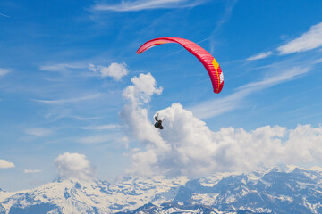 A breathtaking solo paragliding flight over the snow-covered Alpine mountain peaks under a bright blue sky with fluffy white clouds © tatiana
