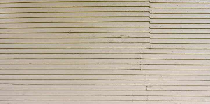 Close up of beige painted beveled lap siding with rough, thick paint, outlines of older paint layers, visible wood grain, misaligned boards, gouges and cracks