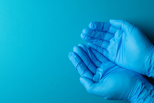 Healthcare and medical protection concept. Cupped hands wearing blue nitrile gloves isolated on a solid blue background with copy space. Hygiene, safety and patient support.
