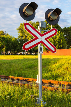 Railway crossing signal post with crossbuck sign and dual traffic lights, railroad track background in summer evening light