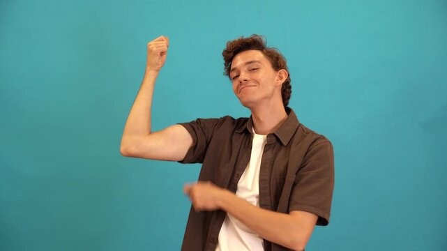 Confident young man flexing and pointing at his bicep against a blue background