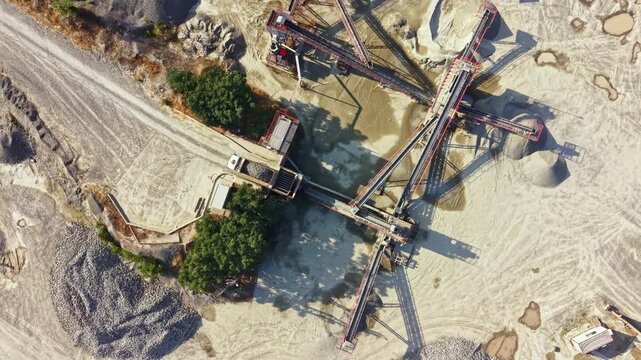 A granite quarry where machines handle stones and materials. Trucks are present, and the landscape consists of piles of stone and equipment working in the area.