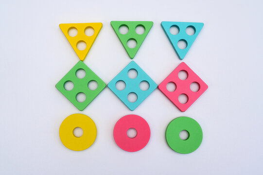 Geometric blocks lie in rows on white background. Wooden sorting toy pieces show triangles squares circles. Educational math puzzle parts stand in pattern for kids learning.