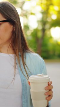 Happy woman with the smartphone and coffee to go stands on the street 