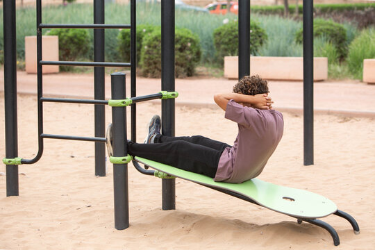 Man Doing Sit-Ups at Outdoor Gym. Teenager doing abdominal exercise on outdoor fitness equipment in a public park