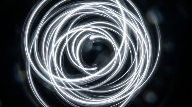 Long exposure shot of swirling white light trails forming circular pattern against deep black space.