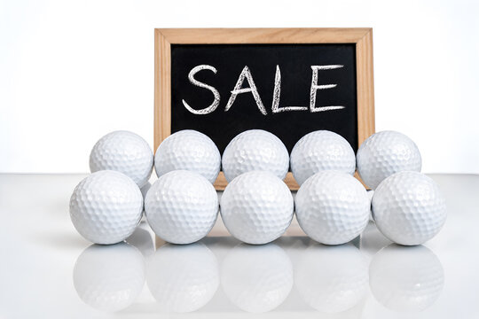 Group of white golf balls displayed on a reflective surface sale sign in background Sports and leisure equipment