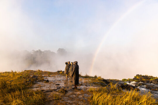  family at edge of Victoria Falls, Zambia, Africa, rainbow in background