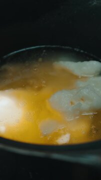 overhead close-up inside dark pot showing warm golden broth gently simmering around pale creamy solids