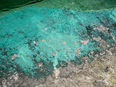 Close-up of a weathered concrete wall with peeling turquoise paint, revealing rough grey plaster texture, cracks, and natural grunge details.
