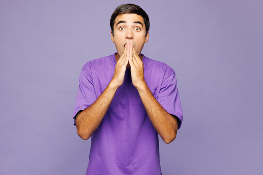 Young shocked surprised fun Caucasian man he wear violet t-shirt casual clothes look camera cover mouth with hands isolated on plain pastel light purple background studio portrait. Lifestyle concept.