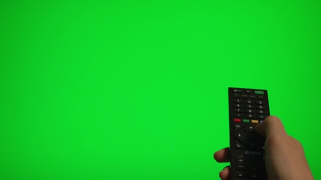 Hand holding remote control pointing at green screen TV mockup.