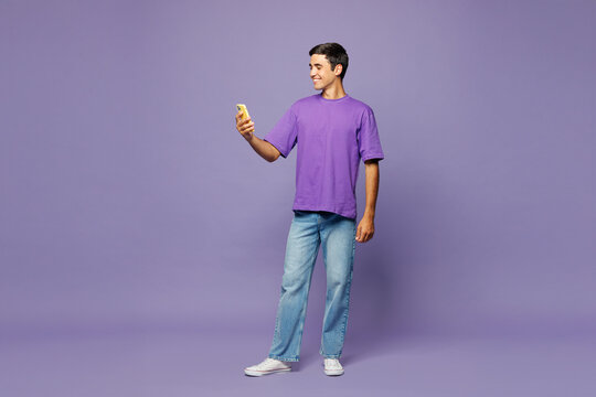Full body young happy man he wear violet t-shirt casual clothes hold in hand use mobile cell phone texting message isolated on plain pastel light purple background studio portrait. Lifestyle concept.