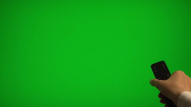 Hand holding remote control pointing at green screen TV mockup.