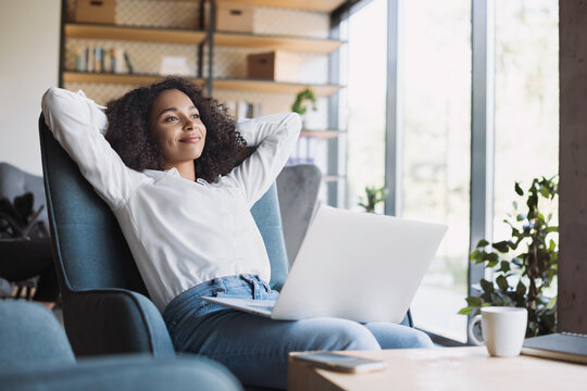 Satisfied young business woman relaxing in an office chair, unwinding after a hard day at work with hands behind her head. Holiday, vacation and business success concept