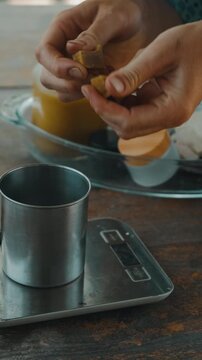 close-up shows hands dropping peeled gherkin pieces into metal cup beside jars on wooden counter near