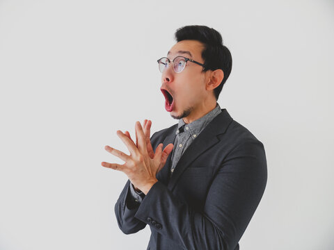 Astonished young Asian man in glasses reacting with wide open mouth and clasped hands