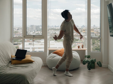 Young man dancing freely in his apartment living room with headphones