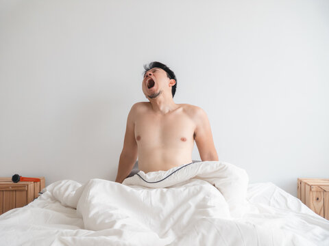 Young Asian Man Yawning Widely While Waking Up in a Comfortable White Bed