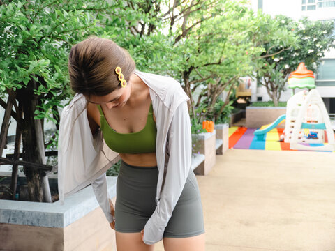 Young Asian Woman in Athletic Wear Adjusting Her Shorts Outdoors Near a Playground