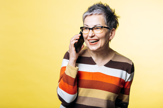 Happy mature woman communicating on mobile phone, showing enjoyment and connectivity against a vibrant yellow background