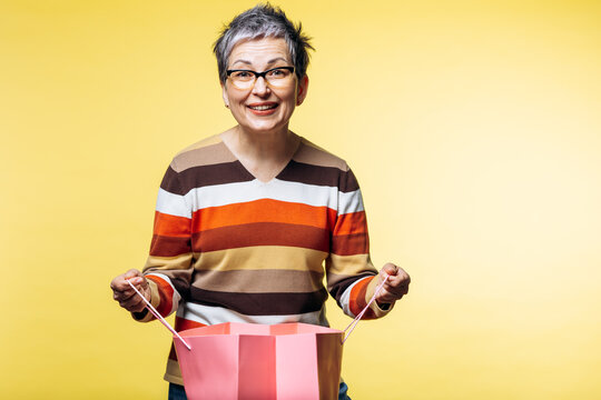 Senior woman with a happy expression opening a pink shopping bag, feeling excitement and joy about her recent purchase or present
