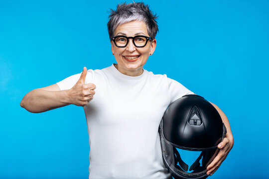 Mature female biker expressing safety and freedom, smiling and holding a helmet against a blue background