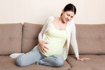 Fototapeta premium Pregnant woman with painful belly on sofa at home