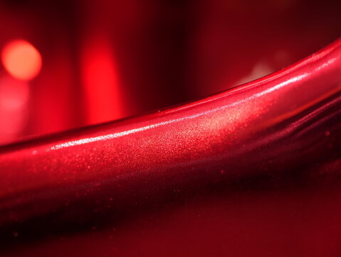 Close-up of a smooth, glossy metallic red surface with a sharp bright highlight line and a soft bokeh background creating an abstract, modern aesthetic.