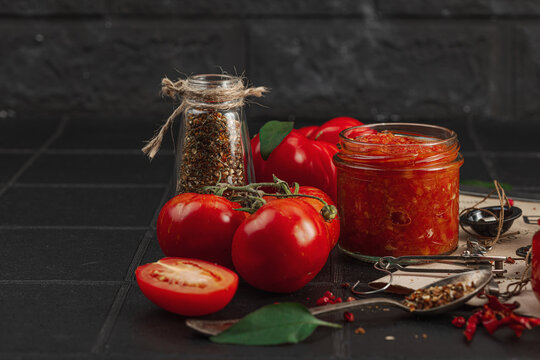 Homemade tomato sauces, ketchup and adjika in glass jars with heirloom tomatoes on dark background