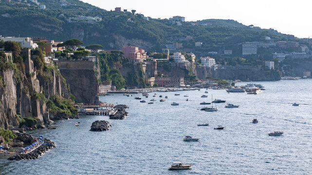Late afternoon summer view from Sant'Agnello, Italy, overlooking the steep tuff cliffs of the Sorrento Peninsula coastline towards Marina Piccola port. Turquoise water filled with moored yachts and bo