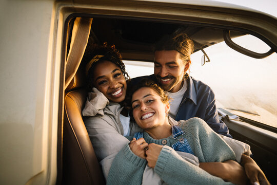 Three friends embracing in a car smiling at the camera