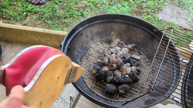 Hand-operated bellows intensifying glowing charcoal on a backyard barbecue, horizontal real time video
