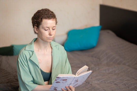 woman with a visible implanted port sits on a bed using a smartphone, showing digital communication, home recovery and daily life during cancer treatment