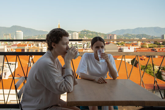 cancer survivor and supportive friend enjoy coffee together on a balcony, sharing laughter, emotional support, recovery friendship and a relaxing travel morning