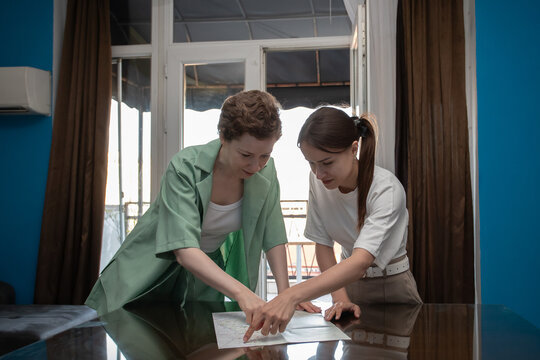 mother and teenage daughter explore a printed map before departure, sharing travel ideas, comparing routes and organizing an independent family trip from their apartment
