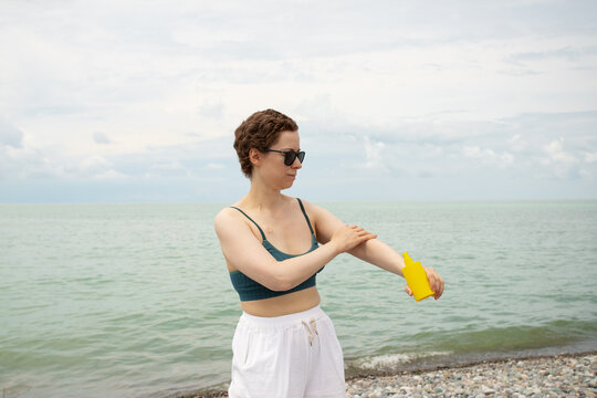 woman recovering from cancer applies sunscreen to her hand on the beach, emphasizing sun protection, healthy skin care and safe summer rehabilitation by the sea