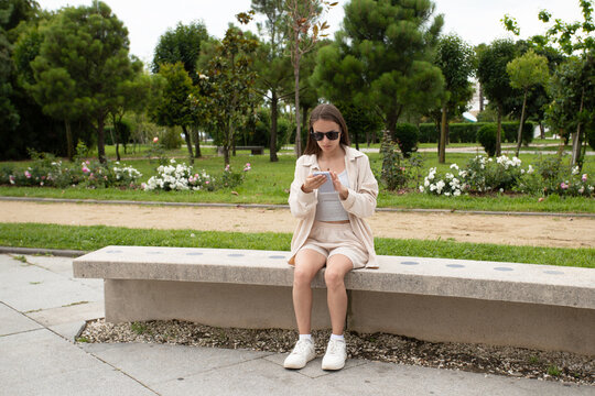 teen girl using a smartphone on a park bench, showing digital habits, city summer lifestyle and outdoor leisure in warm urban weather