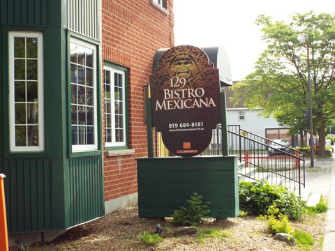 Gatineau,Quebec, Canada &ndash; June 4, 2026: The "129 Bistro Mexicana" exterior features a distinctive restaurant sign, red brick wall, green wooden panels, and street view on Rue Principale.