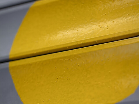 Close-up of a textured yellow painted metal surface with small surface bubbles and a distinct panel gap against a grey background.