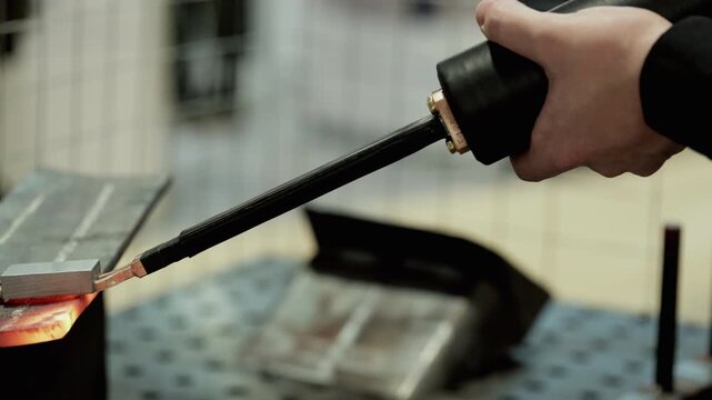 Worker uses portable induction machine to heat steel rods on exhibition display closeup. Presentation of energy efficient metalworking technology in workshop