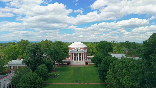 Charlottesville, Virginia, beautiful aerial drone video looking down the historic lush green Lawn toward the iconic University of Virginia Rotunda on a bright, sunny day with scattered clouds.