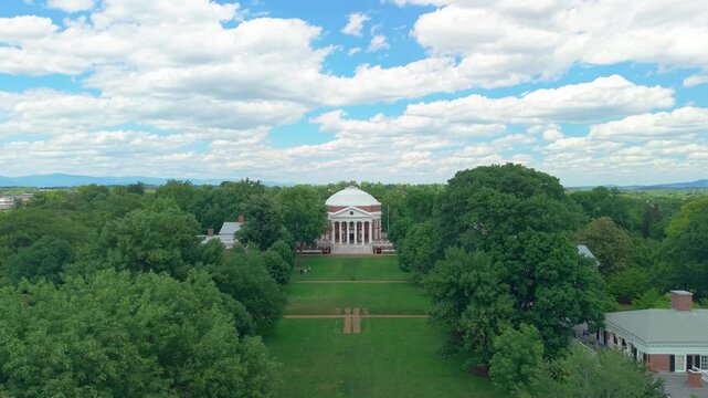 Charlottesville, Virginia, beautiful aerial drone video looking down the historic lush green Lawn toward the iconic University of Virginia Rotunda on a bright, sunny day with scattered clouds.