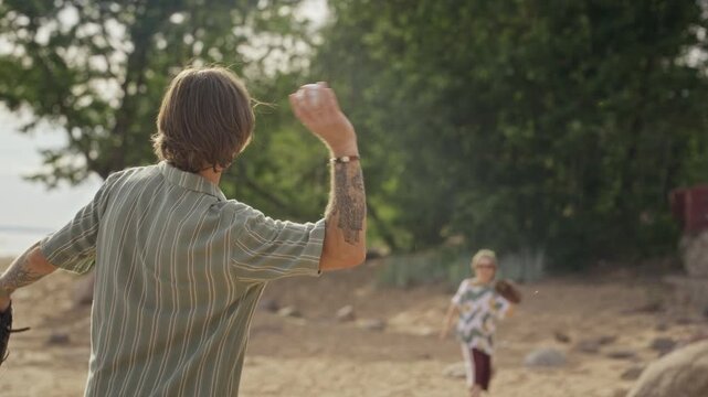 Caucasian father picking up baseball from sand and throwing it to young son on beach. Footage is ideal for family lifestyle commercials and parenting brand advertisements