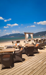 Beachfront cafe in Quy Nhon, Vietnam, with tables, chairs and sunshades overlooking the sea, gentle waves and fishing boats in the background on a sunny day. © Olga Khoroshunova