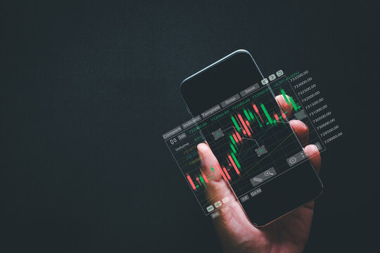 Stock market and mobile trading concept. Hand holding a smartphone with a futuristic glowing candlestick chart overlay on a dark background. Fintech, cryptocurrency and digital investment.